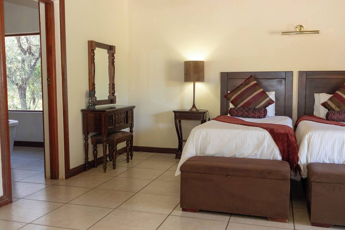 A hotel room with two beds, a dresser, a mirror, a lamp, and a view of the outdoors.