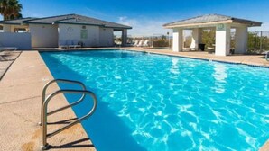Ein klares, blaues Schwimmbecken mit Rettungsschwimmerstuhl, überdachtem Sitzbereich und einem Gebäude mit Beschilderung.