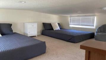 Une chambre avec deux lits, une table de chevet, une fenêtre avec des stores et une petite table en bois.