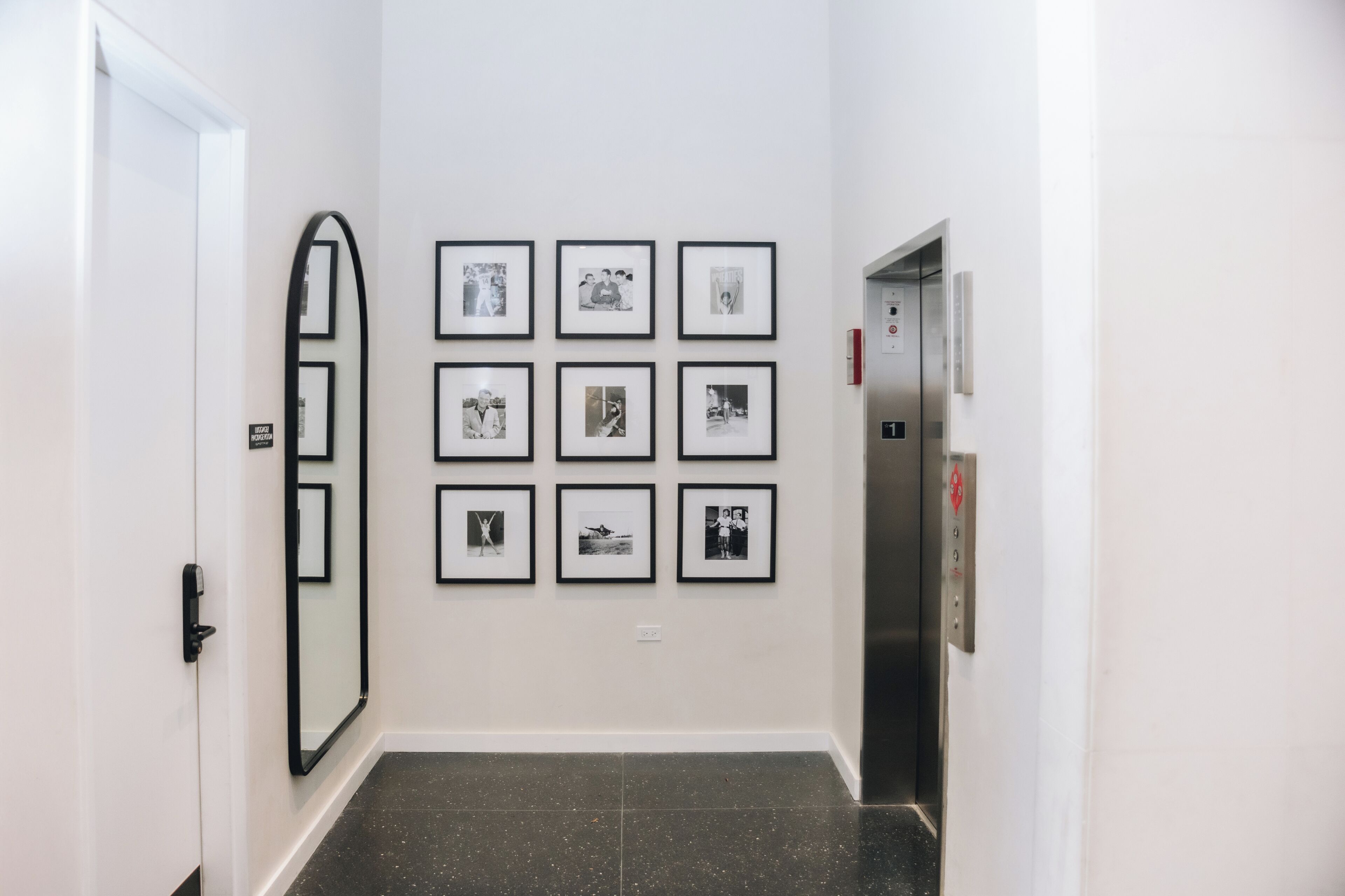 Un couloir orné d’une série de photographies encadrées accrochées au mur, d’un grand miroir et d’un ascenseur.