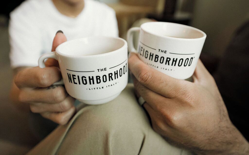 Two white mugs with the text "The Neighborhood" and "Little Italy" on them.