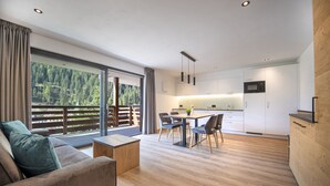 Eine moderne Küche mit weißen Schränken, ein Essbereich mit Tisch und Stühlen sowie eine große Schiebeglasdoor zum Balkon mit Holzboden.