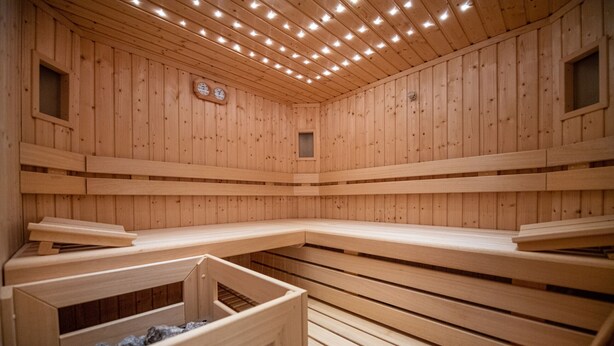 A sauna with wooden walls and benches, a clock, and a small window. - 183A Cristina Hospitality (Ortisei)
