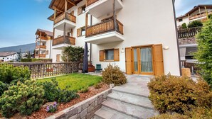 A multi-story residential building with balconies, a stone pathway, and a well-maintained garden. - 183A Cristina Hospitality (Ortisei)