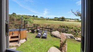 A patio with two lounge chairs, a wooden hot tub, and a stone wall. - Bosulla Shepherds Hut (Penzance)