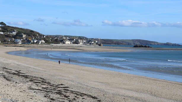 A coastal beach with a sandy shore, a few people walking, and buildings in the background. - Bosulla Shepherds Hut (Penzance)