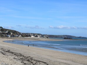 A coastal beach with a sandy shore, a few people walking, and buildings in the background.