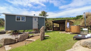 A small, single-story cabin with a metal roof, a wooden deck, and a sauna area. - Bosulla Shepherds Hut (Penzance)