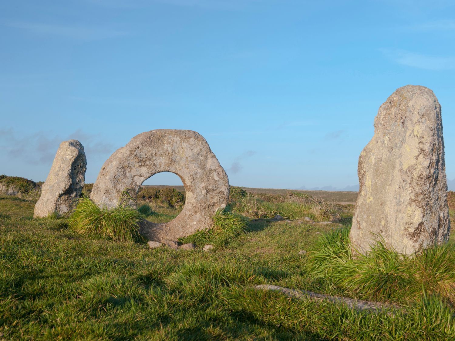 Three large standing stones in a grassy field with a clear sky.