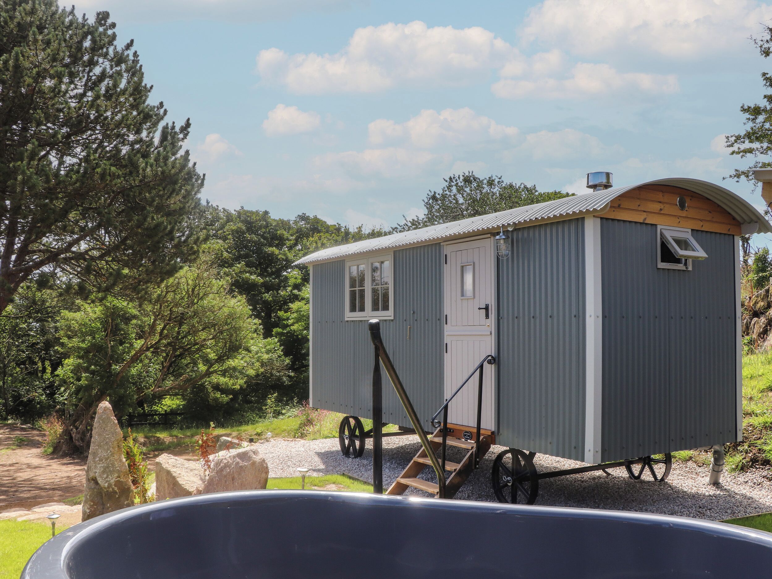 A small, single-room cabin with a door and window, a small porch, and a wheelbarrow in front.