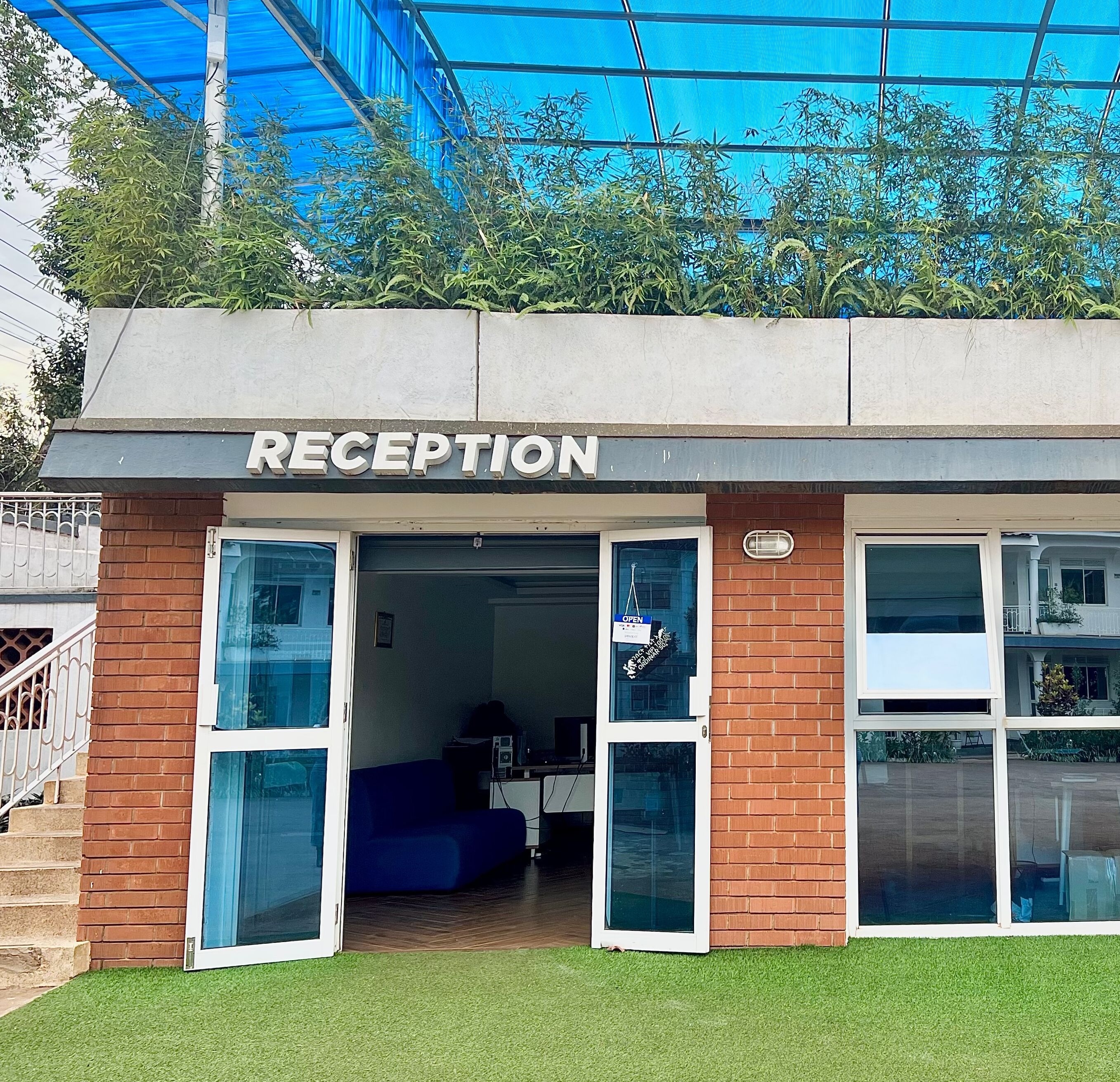 A reception area with a sign above the entrance, a blue couch inside, and a covered outdoor area with plants.