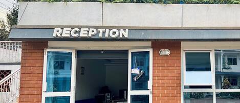 A reception area with a sign above the entrance, a blue couch inside, and a covered outdoor area with plants.