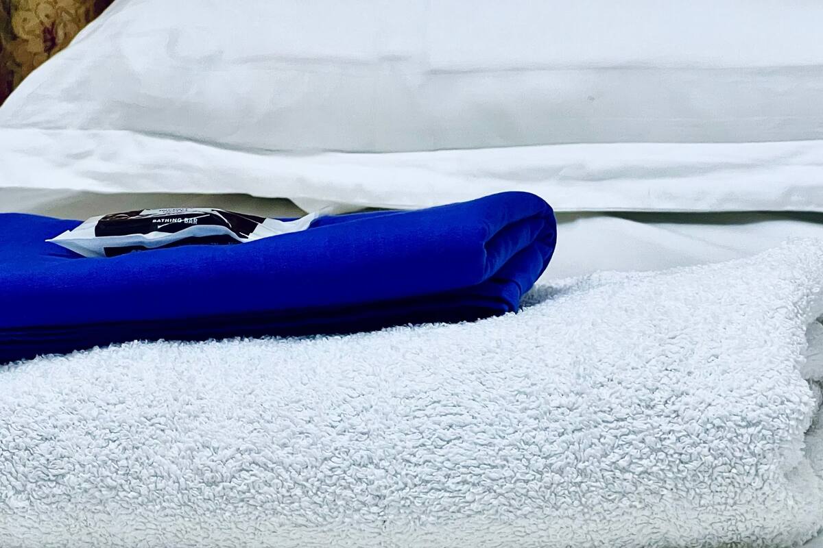 A neatly made bed with white linens and a folded blue towel.
