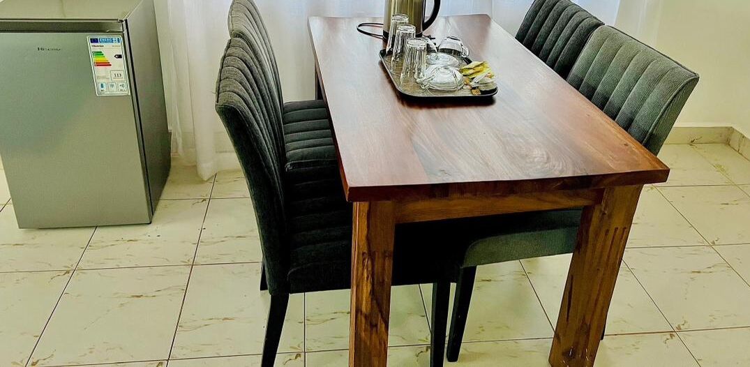 A dining area with a wooden table, black upholstered chairs, and a small refrigerator.