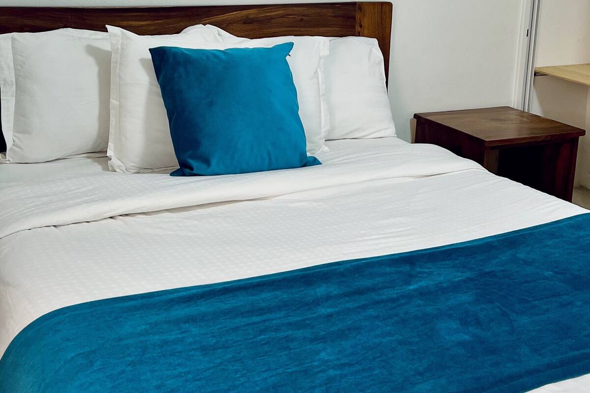 A neatly made bed with white bedding and a blue throw blanket.