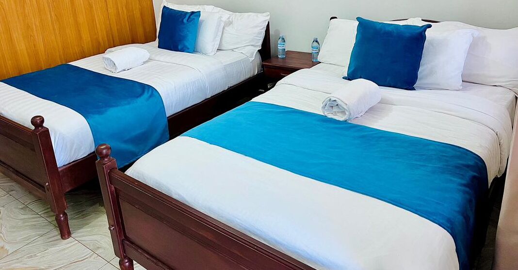 Two twin beds with wooden frames, white bedding, and blue accents. Each bed has a water bottle on the nightstand.
