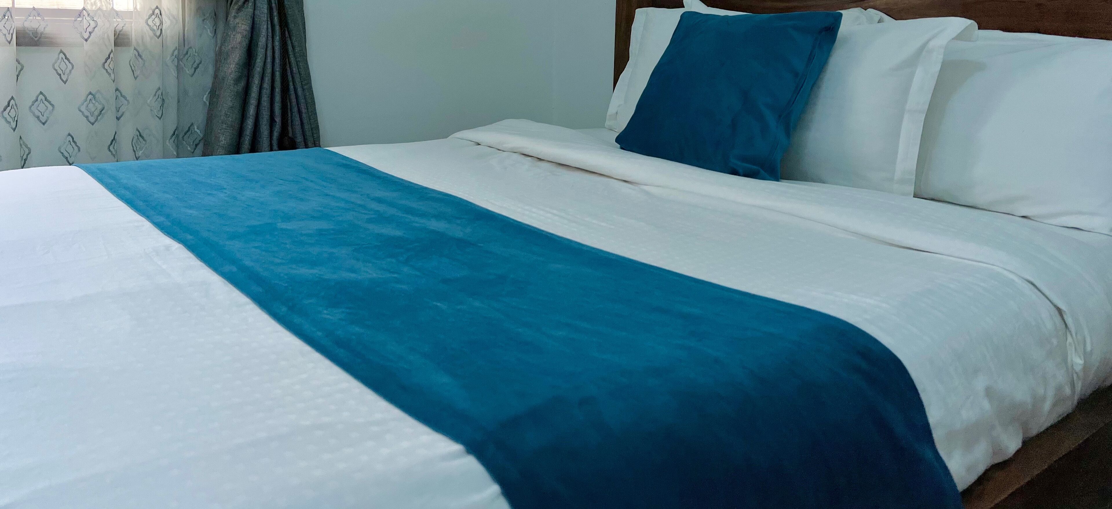 A neatly made bed with a blue and white bedspread, white pillows, and a wooden headboard.