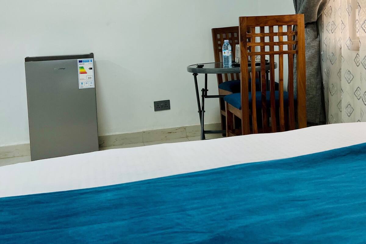 A bedroom with a bed, a small table, a chair, a refrigerator, and a patterned curtain.