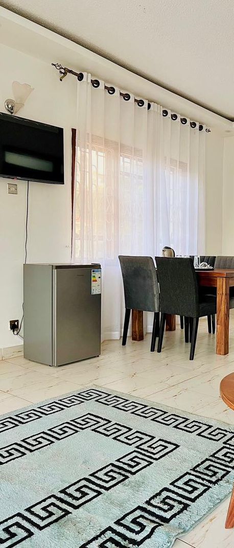 Une pièce comprenant une table à manger, des chaises, un téléviseur fixé au mur et un réfrigérateur.
