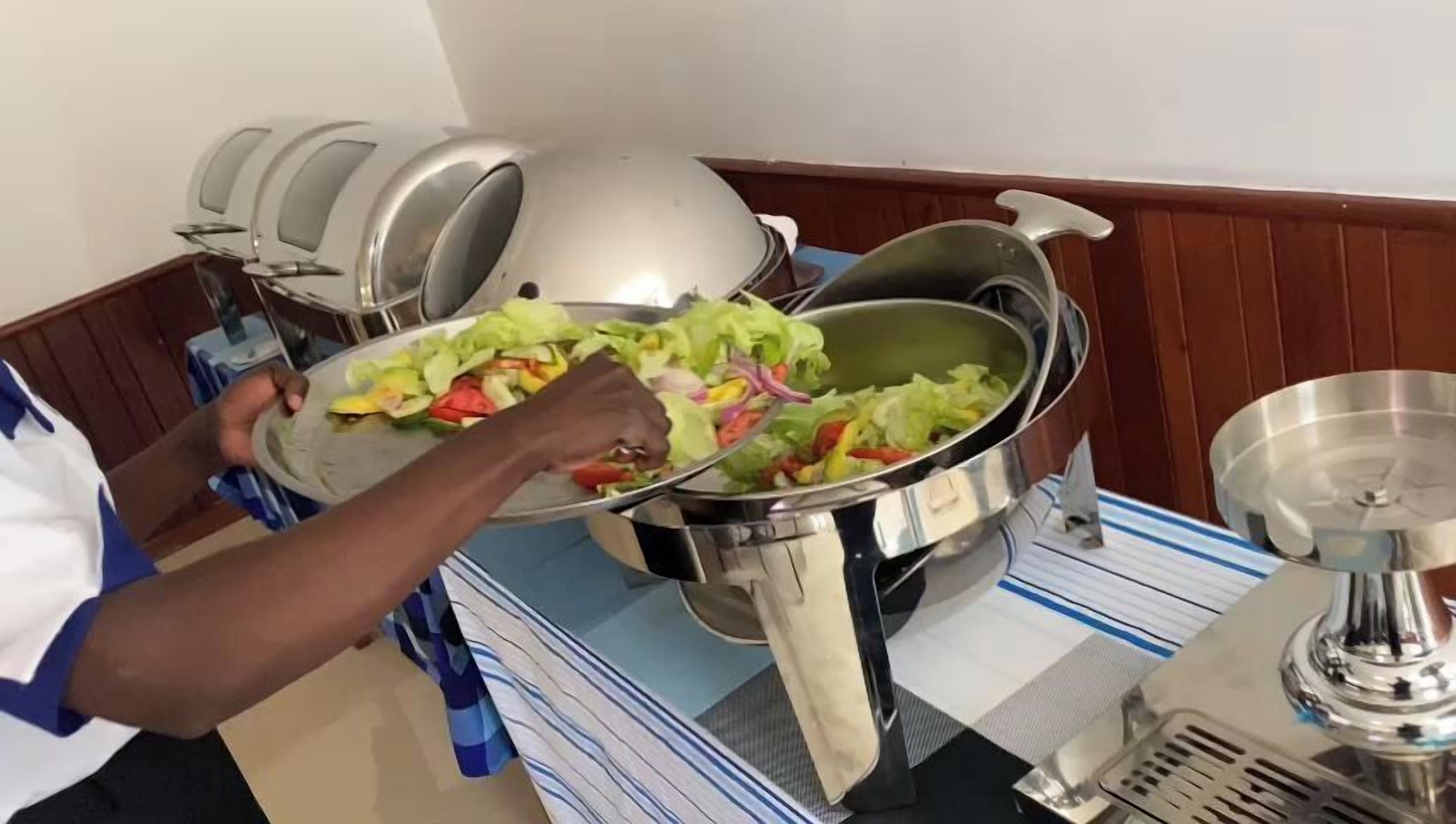 A person serving a salad from a large metal pot to a plate.