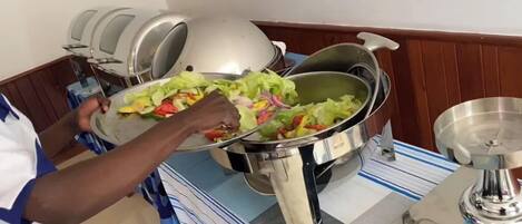 A person serving a salad from a large metal pot to a plate.