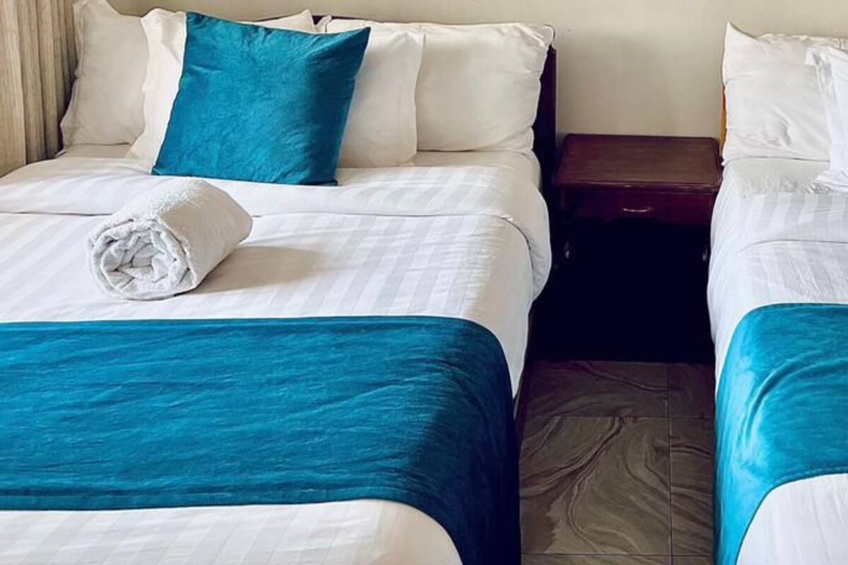 Two twin beds with blue and white bedding, a wooden nightstand, and a rolled white towel on each bed.