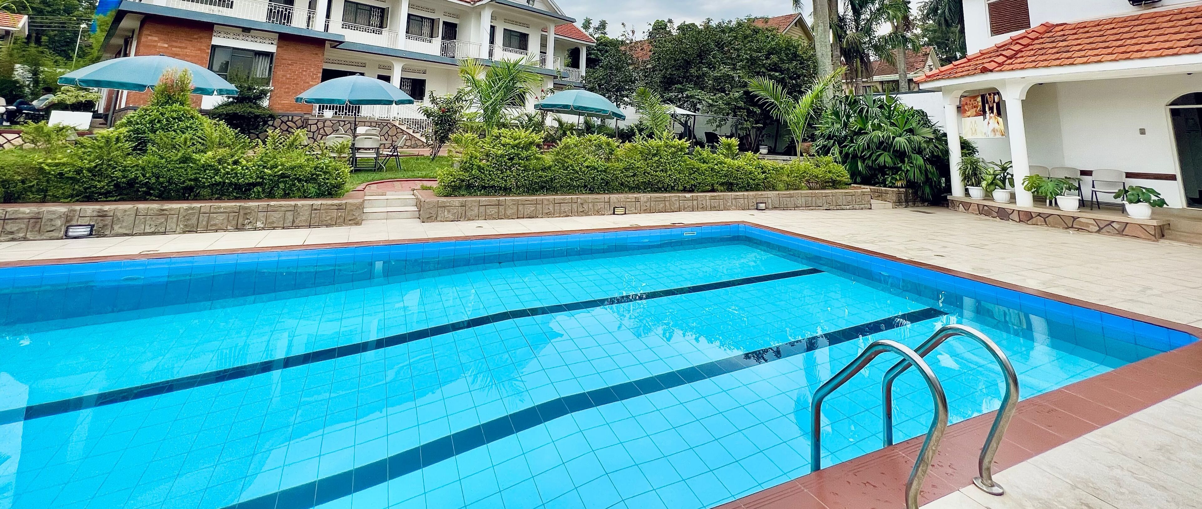 A swimming pool with clear blue water, surrounded by a tiled deck and lush greenery.