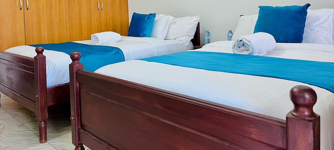 A hotel room with two wooden beds, each with a blue bedspread and white linens.