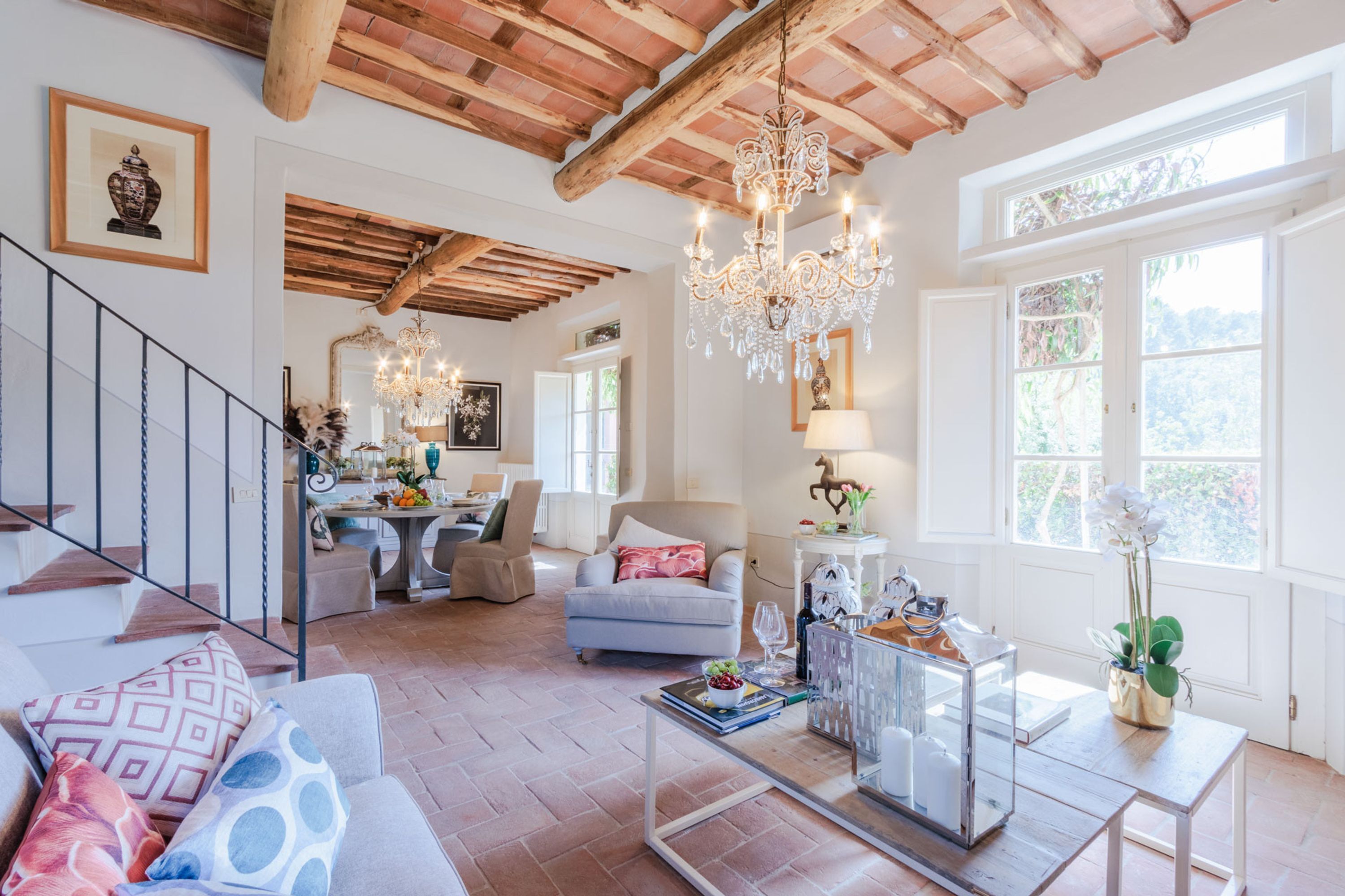 A spacious living area with a wooden ceiling, a chandelier, a dining area, and large windows.