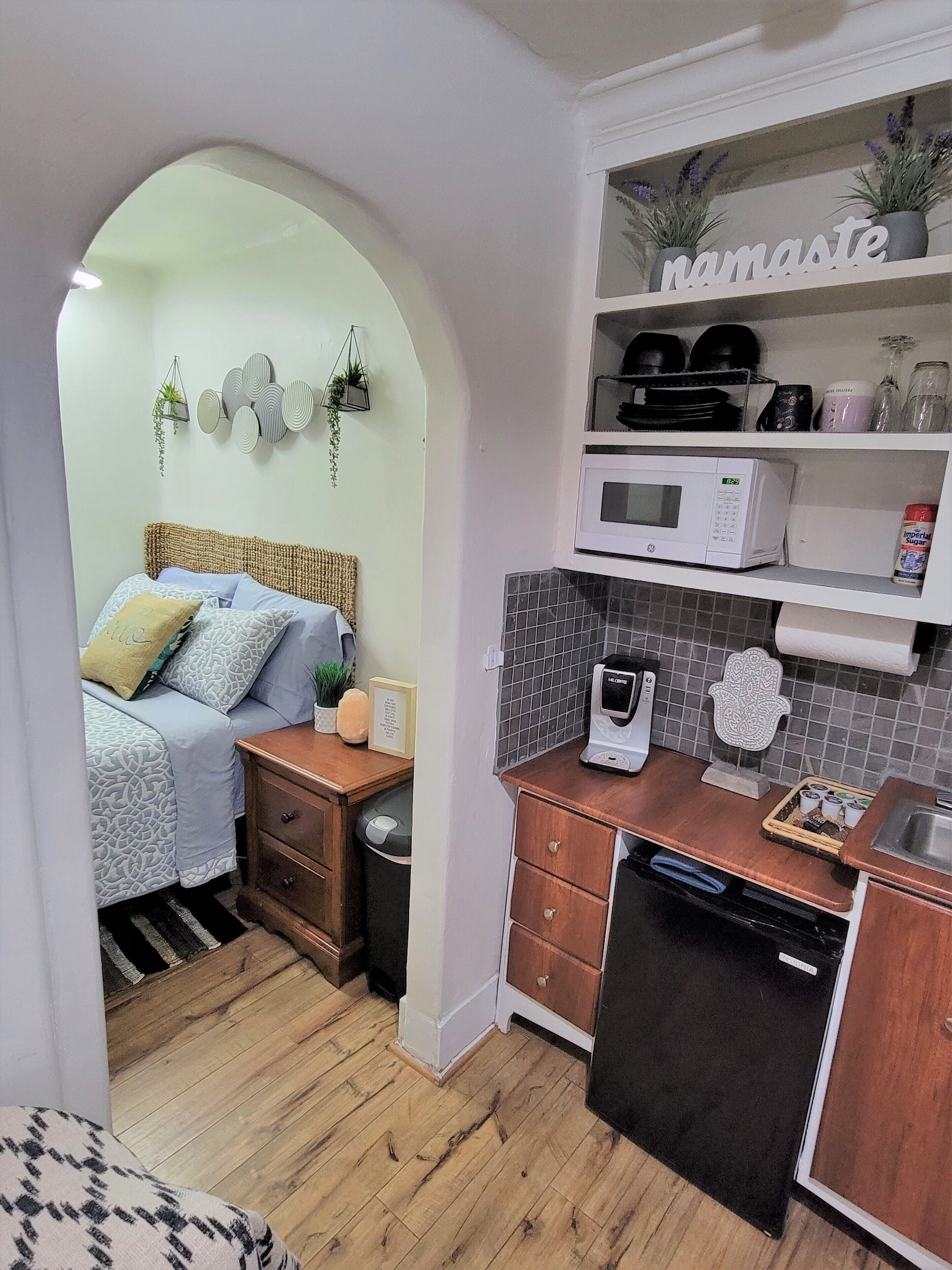 A compact kitchen with a microwave, coffee maker, and a shelf with kitchen items.