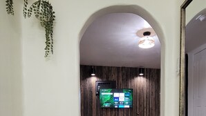 Hotellihuone, jossa on sänky, puinen yöpöytä, puuseinälle asennettu televisio ja käytävä, joka johtaa ovelle.