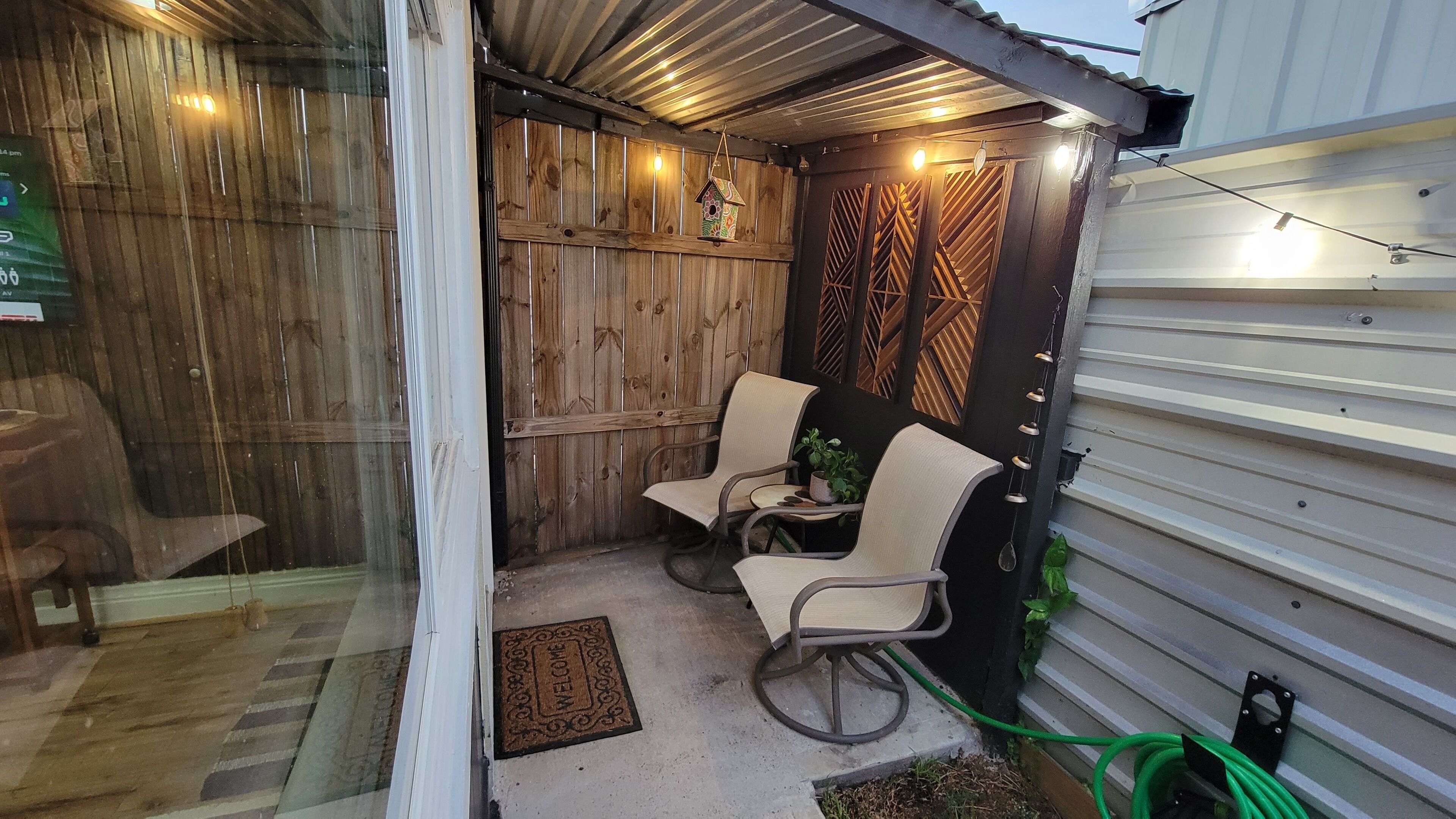 A small outdoor seating area with two chairs and a table, a wooden wall, and a metal gate.