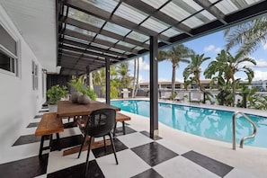 A covered outdoor area with a pool, a wooden table, and chairs.