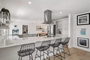 A modern kitchen with a central island, bar stools, stainless steel appliances, and a hanging plant. - Seasons in the Sun - Cocoa Beach, Florida (Cocoa Beach)