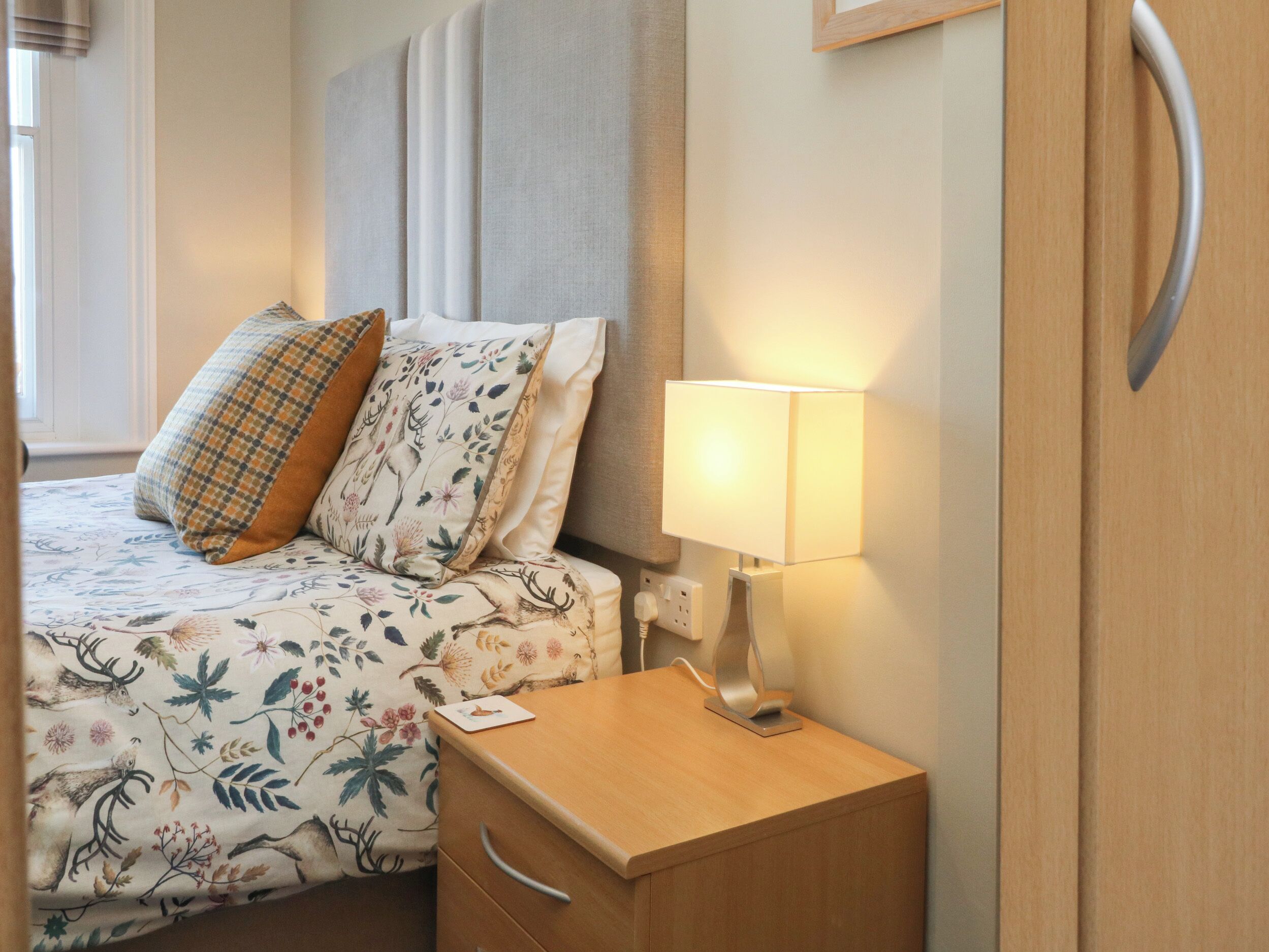 Un lit bien fait, avec une literie à motifs floraux, une lampe de chevet et une table de chevet en bois.