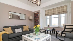 A living room with a sofa, a coffee table with magazines, a bookshelf, and a window with a view. - The Outlook (Minehead)
