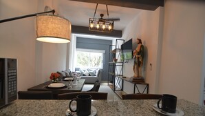 A modern kitchen with granite countertops, a dining area with a sofa, and a TV mounted on the wall. - Condo near Gourmet District + Pool 1BD Unit1
 (Puerto Vallarta)