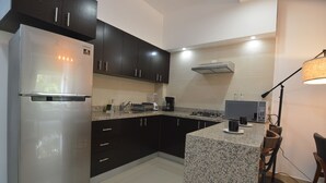 A modern kitchen with dark cabinets, a stainless steel refrigerator, a granite countertop, a coffee maker, and a microwave. - Condo near Gourmet District + Pool 1BD Unit1
 (Puerto Vallarta)
