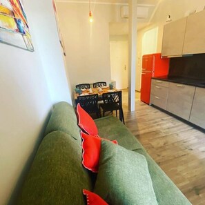 Uma sala de estar com um sofá verde, uma mesa de jantar com cadeiras e uma área de cozinha com armários e uma geladeira.