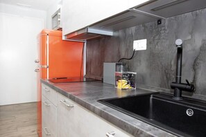 Uma cozinha moderna com pia preta, geladeira vermelha e um recipiente transparente na bancada.