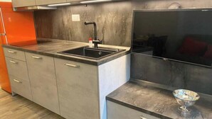 Een moderne keuken met grijze kastjes, een zwarte gootsteen en een achterwand van roestvrij staal.