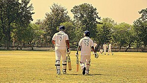 Two cricket players walking on a field with trees in the background. - dfdfdfdfdfdf (Amritsar)