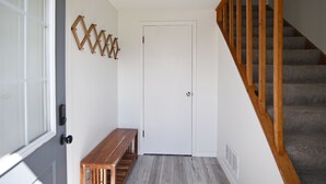 Un couloir avec un banc en bois, une porte blanche et un escalier doté de rampes en bois.