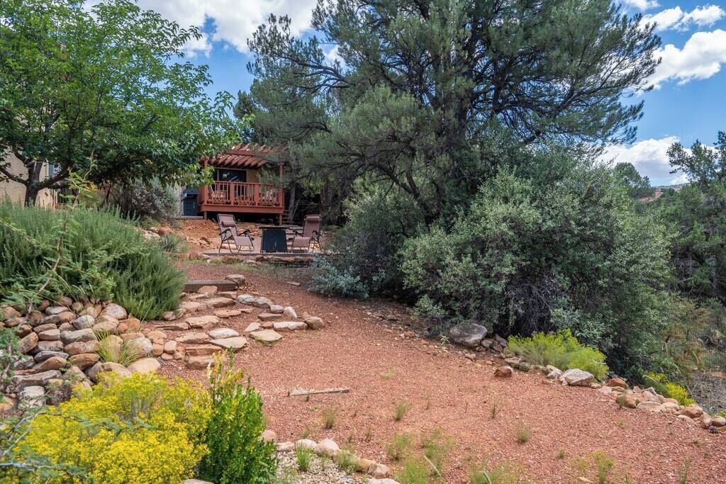 A rustic cabin with a wooden deck and stone pathway surrounded by dense vegetation and trees.
