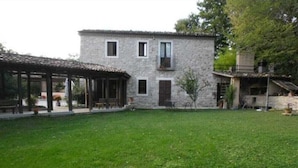 A stone building with a covered patio area and a grassy courtyard. - Casale Cipriani (Casalciprano)