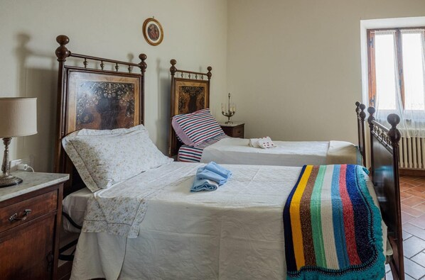 A bedroom with two beds, a nightstand, a lamp, and a picture frame on the wall. - LA CASA IN PIAZZA (Panicale)
