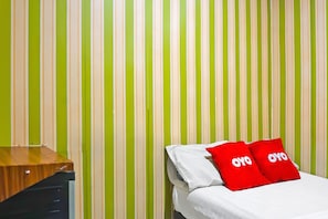 Une pièce avec un mur à rayures vertes et blanches, un bureau en bois et un lit avec des oreillers rouges.