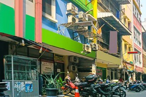 Une rangée de motos est garée devant un immeuble aux façades colorées, équipé de climatiseurs.