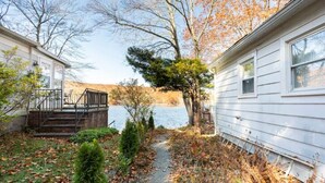 A cabin with a pathway leading to a lake, surrounded by trees and a small garden. - Lakefront Designer House in Pine Plains, NY. (Pine Plains)