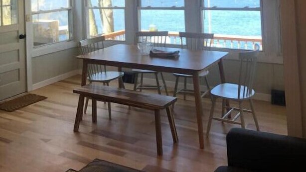 A spacious room with a wooden ceiling, large windows overlooking a body of water, a dining table with chairs, and a bench. - Lakefront Designer House in Pine Plains, NY. (Pine Plains)